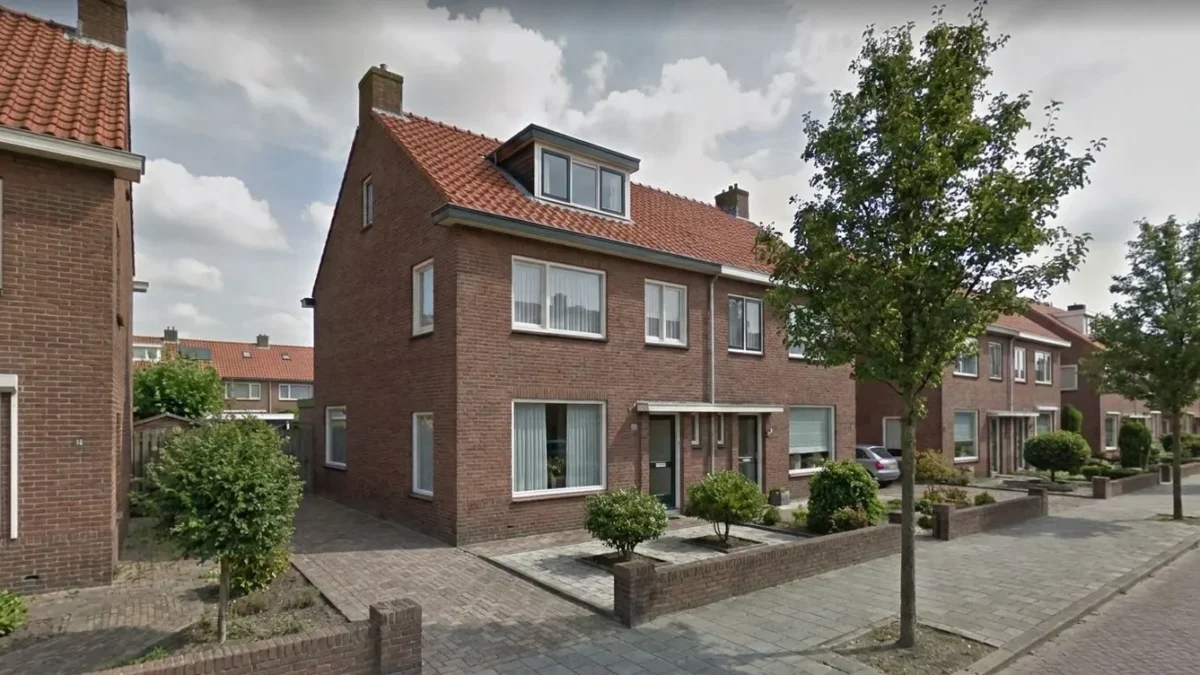 Bakstenen rijtjeshuis met dakkapel en rood pannendak in een woonwijk met geplaveide voortuin.