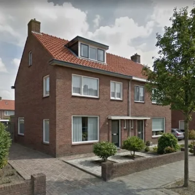 Bakstenen rijtjeshuis met dakkapel en rood pannendak in een woonwijk met geplaveide voortuin.